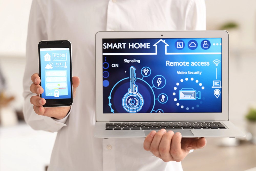 Person demonstrating smart home system on laptop and smartphone simultaneously