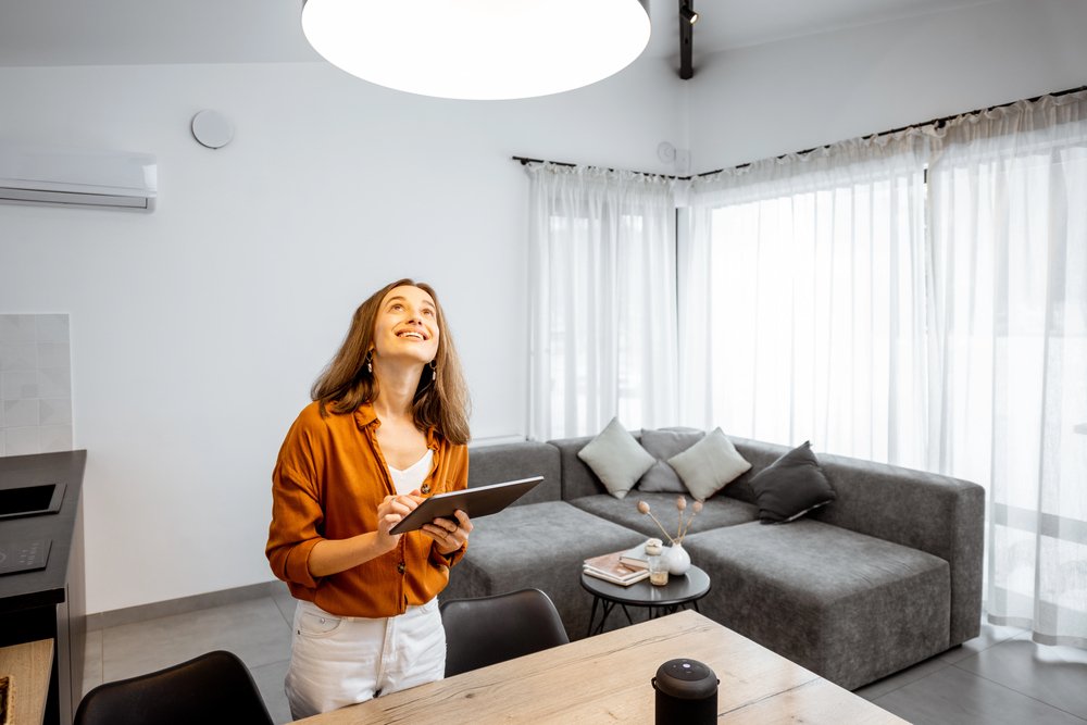 Woman using tablet to control smart ceiling lighting in modern living room